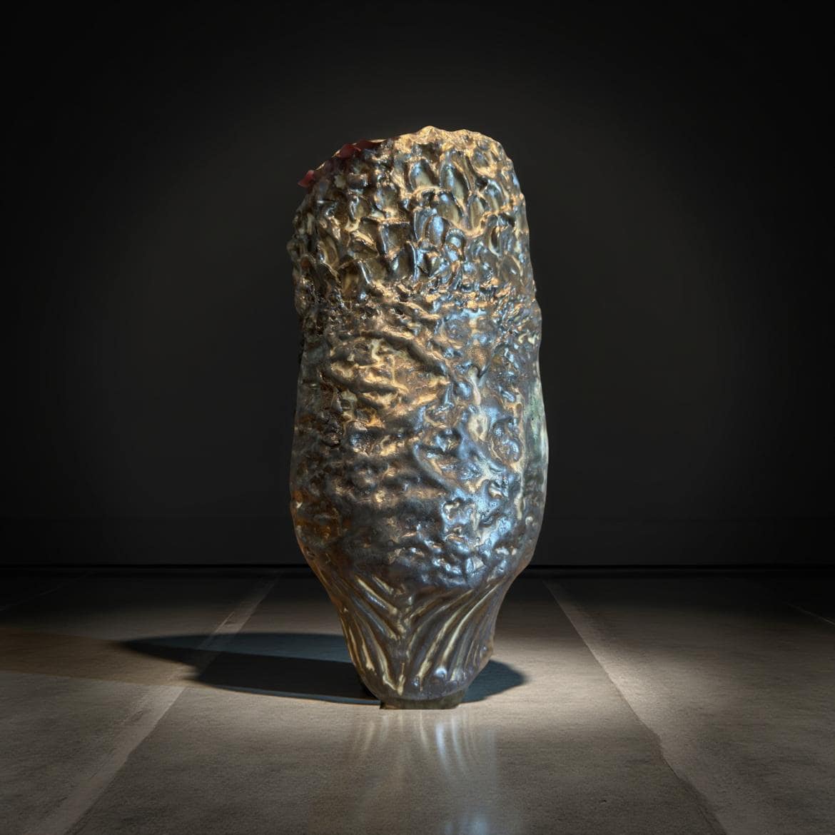 A dark bronze ceramic vase with a textured, organic surface. The vase's form is reminiscent of a stylized flower or plant, with a bulbous body tapering to a slightly flared base. The surface displays a multitude of small, irregular bumps and crevices, creating a rough, almost rocky texture.  The color is a deep, dark bronze with hints of lighter, almost golden tones in the crevices. The overall style is modern and artistic, suggesting a handcrafted or sculptural piece.