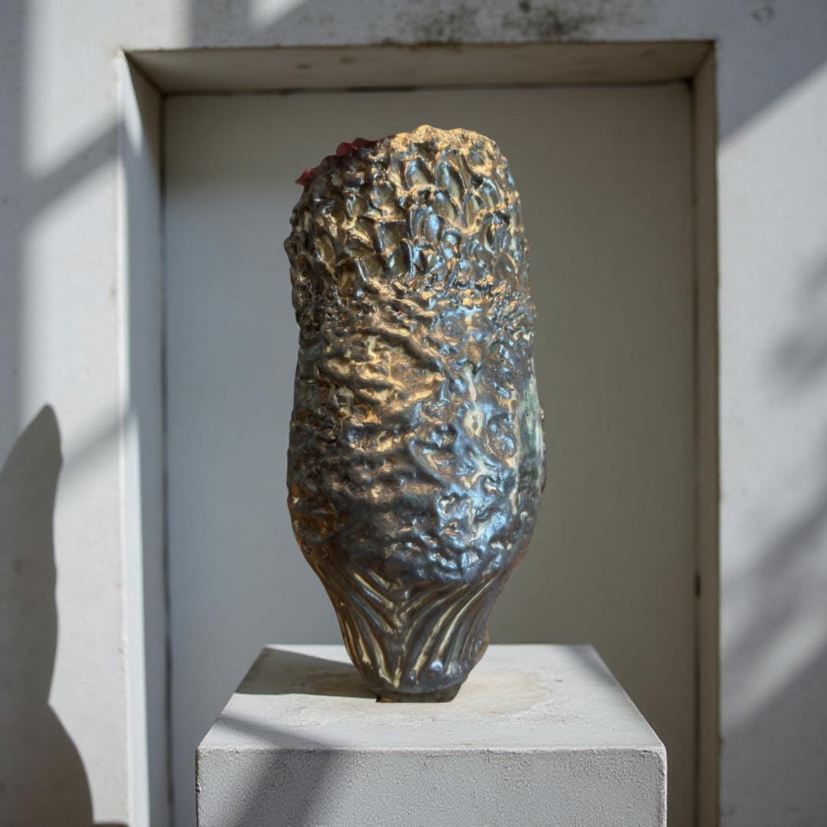 Close-up of a gold-toned ceramic sculpture resembling a stylized corn cob or pod. The surface is textured with numerous small, raised bumps, creating a rough, organic look. The color is a rich, metallic gold with subtle variations in tone and highlights. The base of the sculpture shows fine, vertical lines. The piece appears to be handcrafted and has a unique, artistic design.