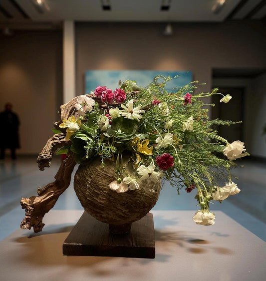 This floral sculpture was arranged in a ceramic vessel I hand-built and fired myself — rough, earthy, imperfect.
Driftwood curls from its side like a memory from the forest.
Every flower was placed by feel — not by rule.
White butterfly blooms, deep pink mini carnations, soft yellow alstroemeria, succulents, sweet peas…
All nestled in wild greenery